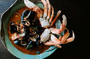 Taylor Shellfish Cioppino Kit cooks up to this – Crab and mussels emerging from a tomato -based sugo in a pale blue bowl