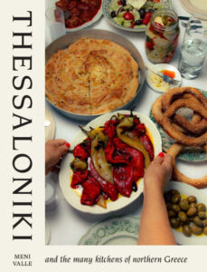 Thessaloniki cookbook cover, by Meni Valle shows a table full of dishes and an arm laying down a plate of peppers and octopus
