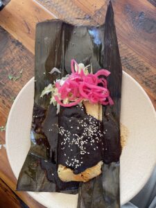 Tamale wrapped in a banana leaf with chocolate mole and pink pickled onions at Sonoma Eats